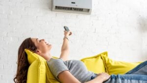 attractive young woman relaxing under air conditioner and holding remote control