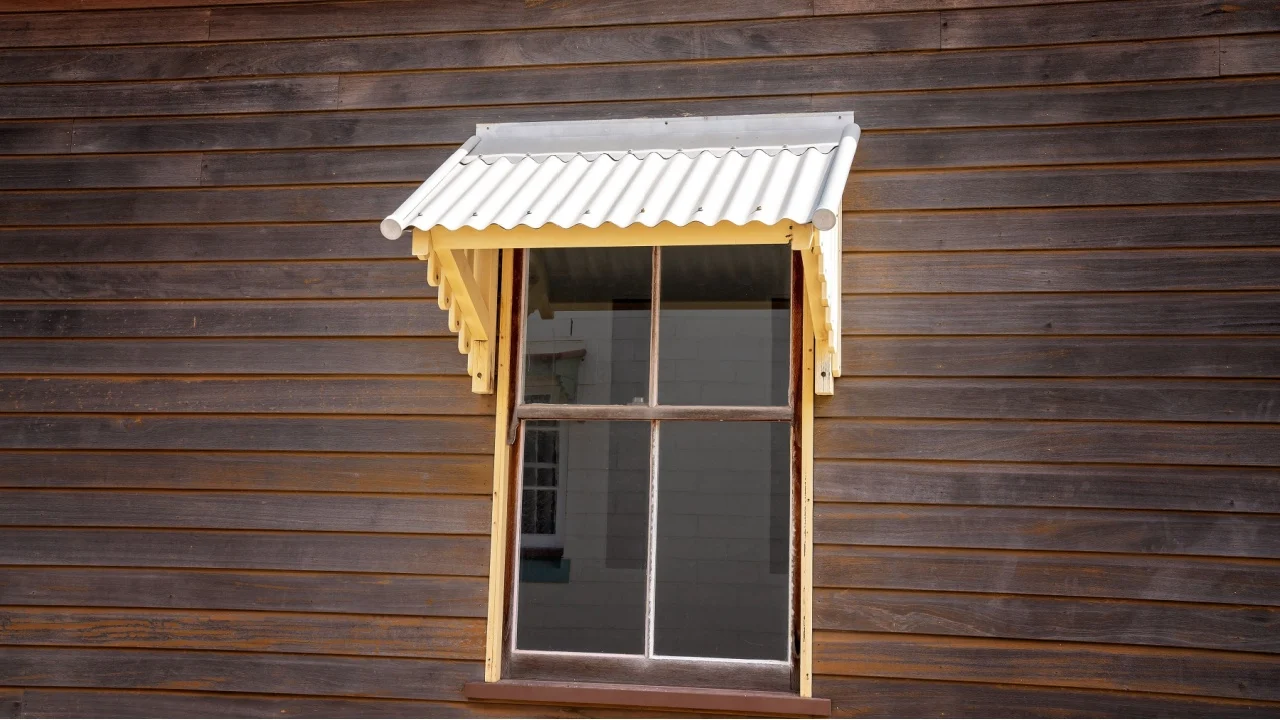 Old fashioned metal window awning on the side of a wooden house