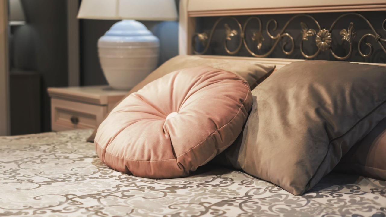 Classic style bed with velvet pillows on floral design bedspread. Fragment of bedroom interior in classic style, evening lighting