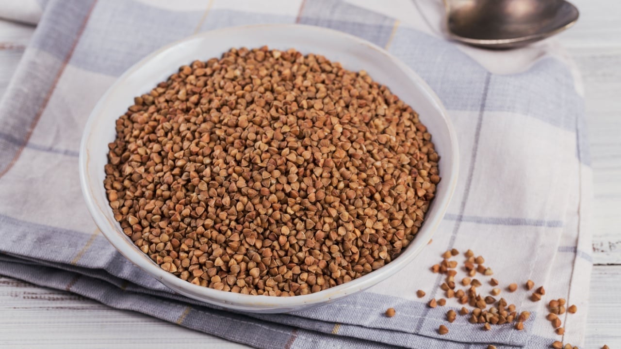 Bowl of dry raw buckwheat groats on white wooden background. Cooking buckwheat porridge concept.