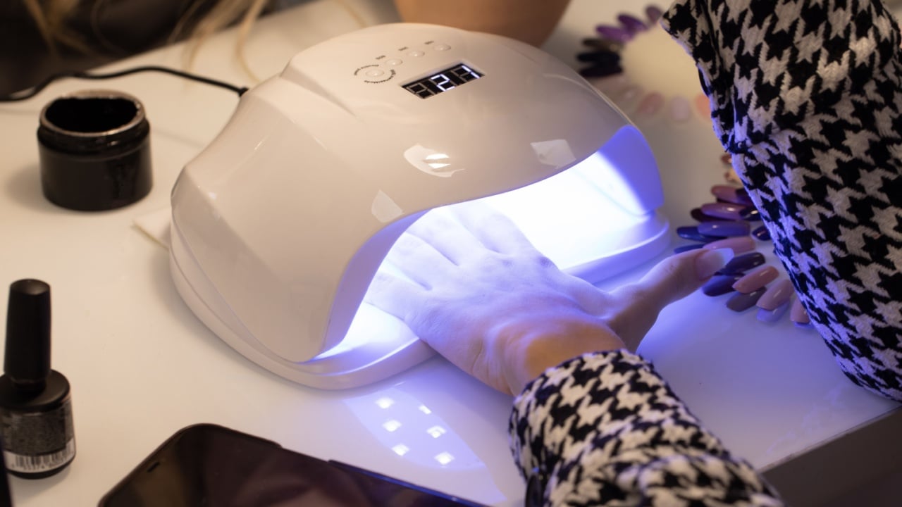 Closeup view of female hands with fresh beautiful modern gel polish manicure. Woman puts hand into led uv lamp for curing top cover of nail polish.