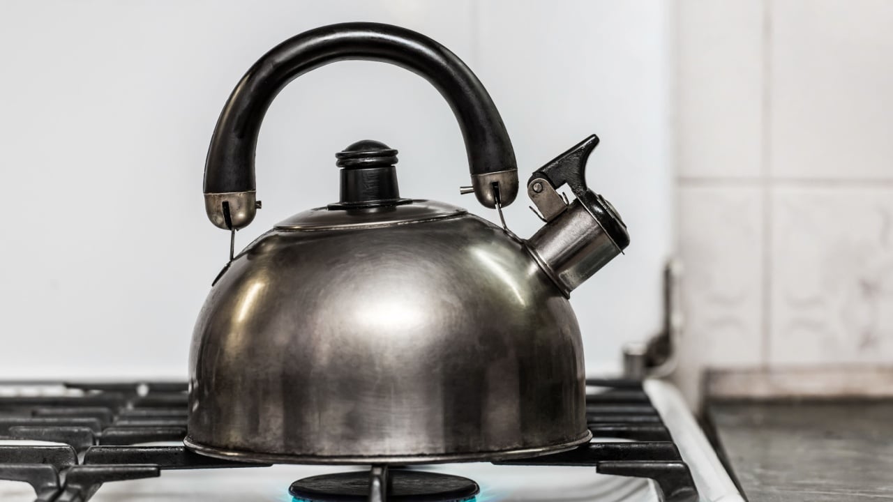 A metal dark kettle with a whistle heats the water to a boil on a gas stove in the kitchen.
