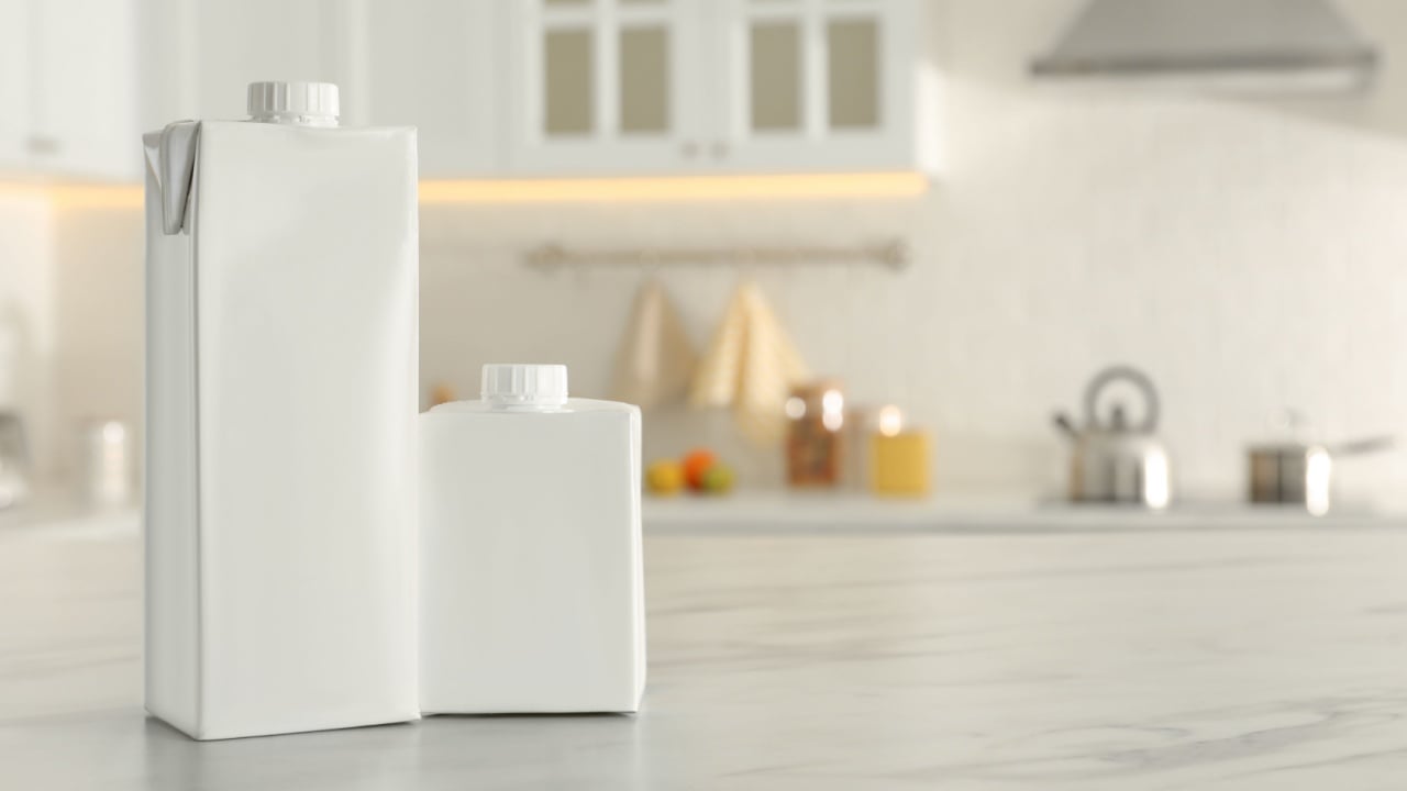 Carton boxes of milk on table in kitchen, space for text