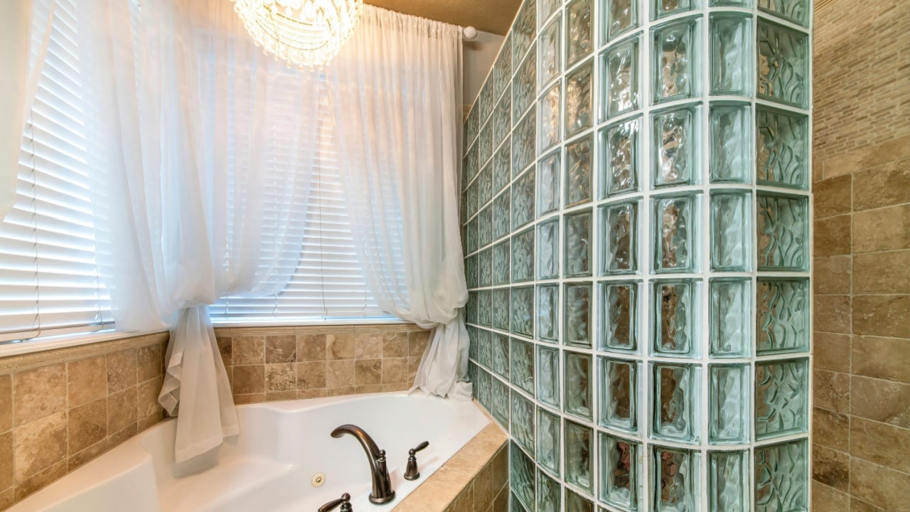 Bathroom interior with corner bathtub and stall with glass block wall