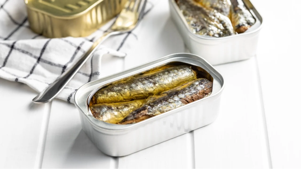 Canned sardines. Sea fish in tin can on white wooden table.