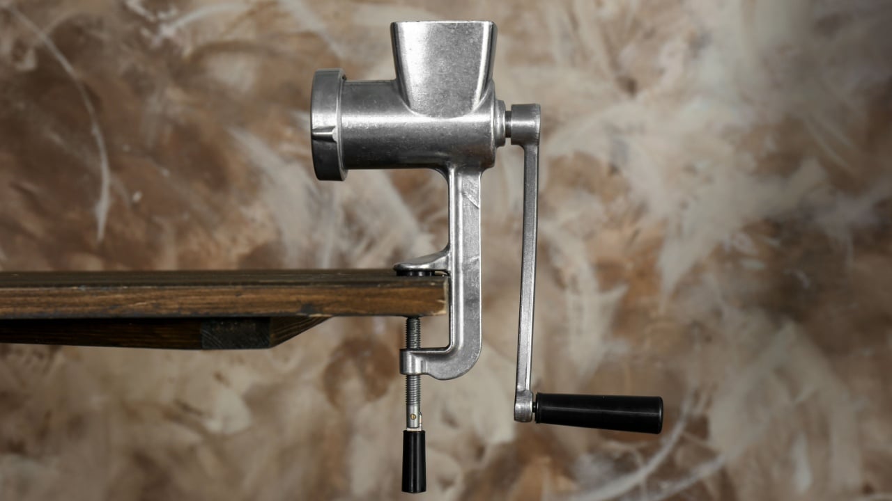 Metal manual meat grinder on wooden table against color background