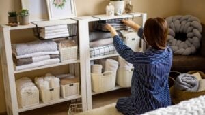 Domestic woman in pajamas neatly putting folded linens into cupboard vertical storage system use Marie Kondo method. Female housewife spring seasonal cleaning space organizer with organized boxes