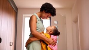 Daughter At Home Hugging Mother As She Helps Her To Get Ready For School
