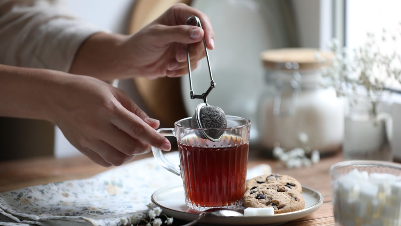 Young woman using snap infuser for brewing tea at wooden table.