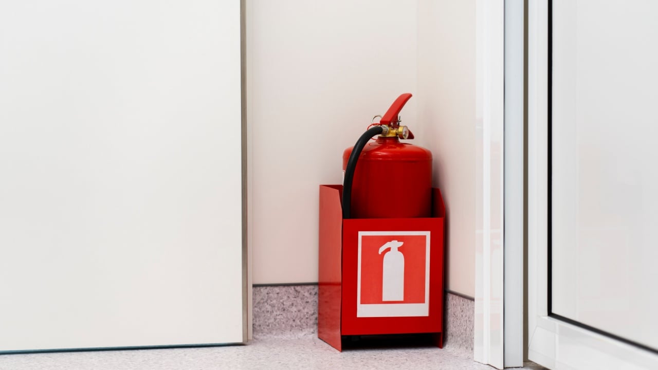 Red fire extinguisher stands in the corner of the room. Life safety concept.