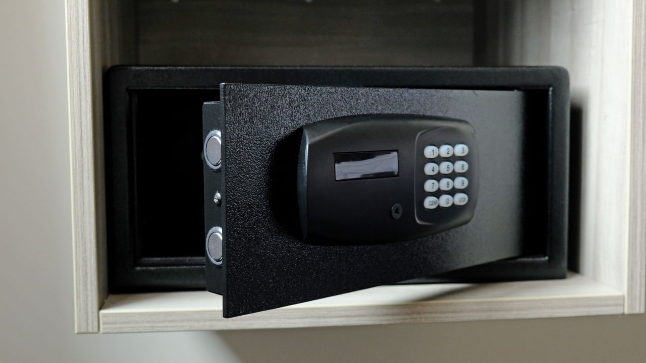 Metal safe box in the closet. Small narrow safe for keeping money or valuables in the hotel. Empty Open safe door with buttons for entering password. Compact strongbox inside cabinet. Selective focus.