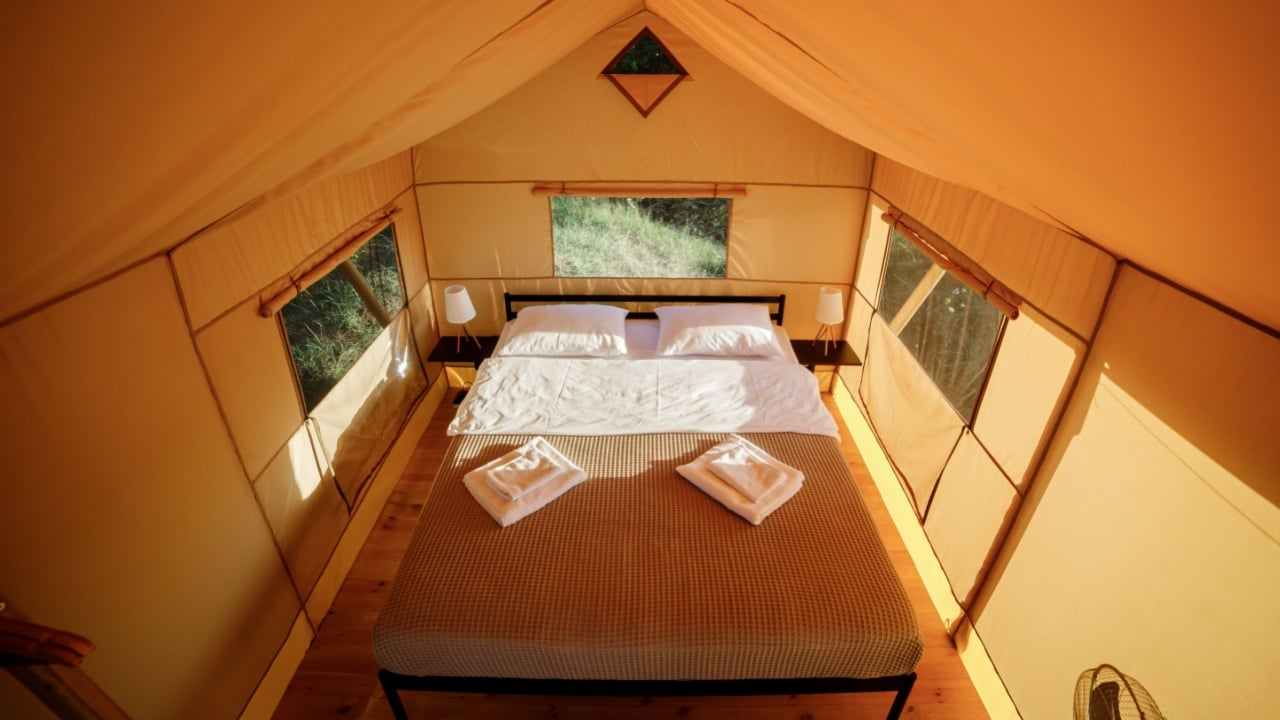 Interior of Cozy open glamping tent with light inside during sunset. Luxury camping tent for outdoor summer holiday and vacation. Lifestyle concept