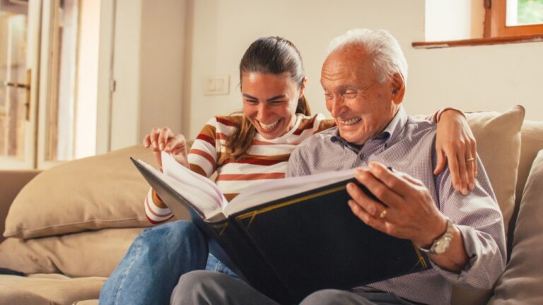 Portrait of a Nostalgic Woman Bringing the Family Photo Album to her Senior Father so They Can Watch Photos Together. Old Man Sharing Memories and Stories with his Daughter in a Bonding Moment