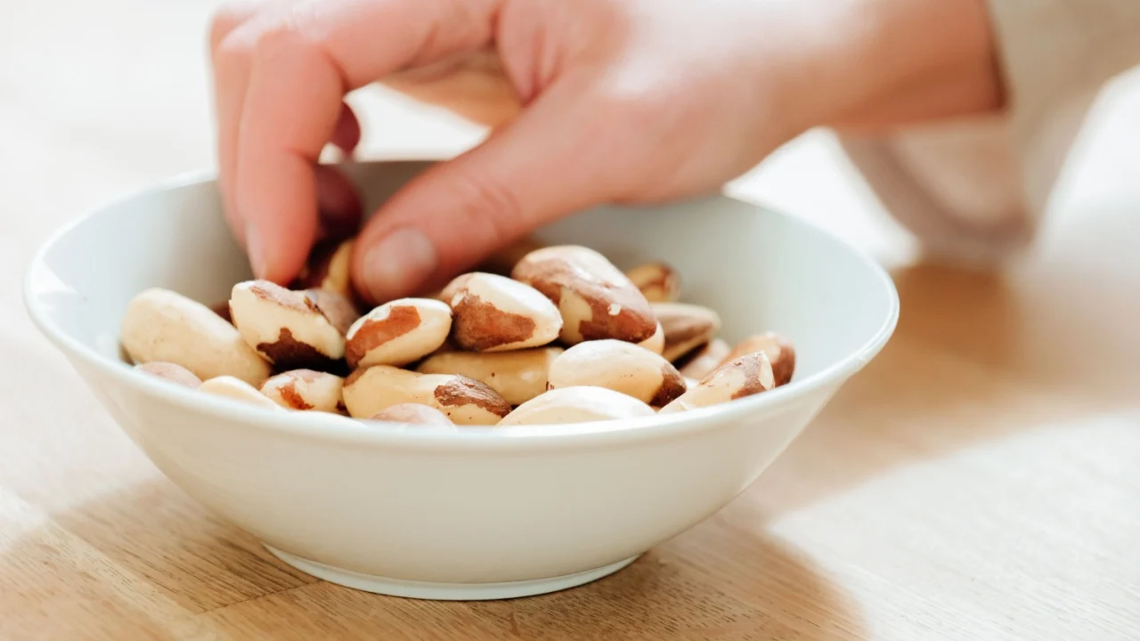Nuts.Brazil nuts cup in hand on a wooden table. Healthy fats in the diet. hand takes brazil nuts from a plate close-up.Useful healthy snack. Brazil nuts in the diet.