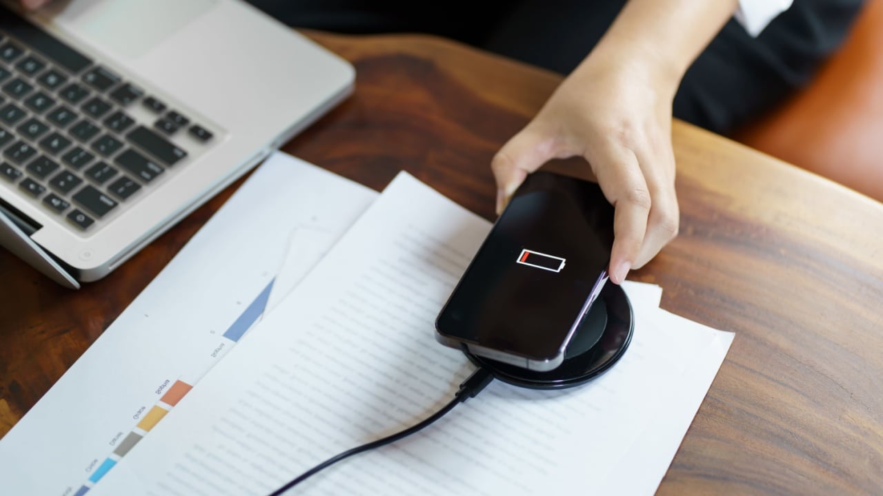 Charging mobile phone battery with wireless charging device in the table. Smartphone charging on a charging pad. Mobile phone near wireless charger Modern lifestyle technology concept.