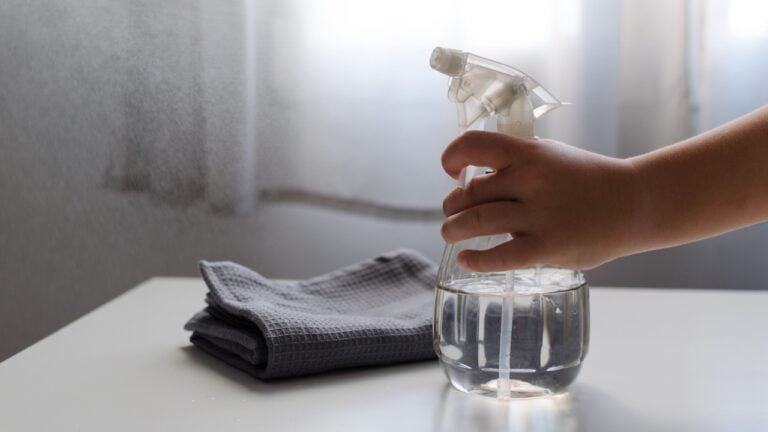 Child's hand squeezing eco cleaning bottle spray filled with water and vinegar. Concept of environmentally friendly home and zero waste, recycling and natural lifestyle