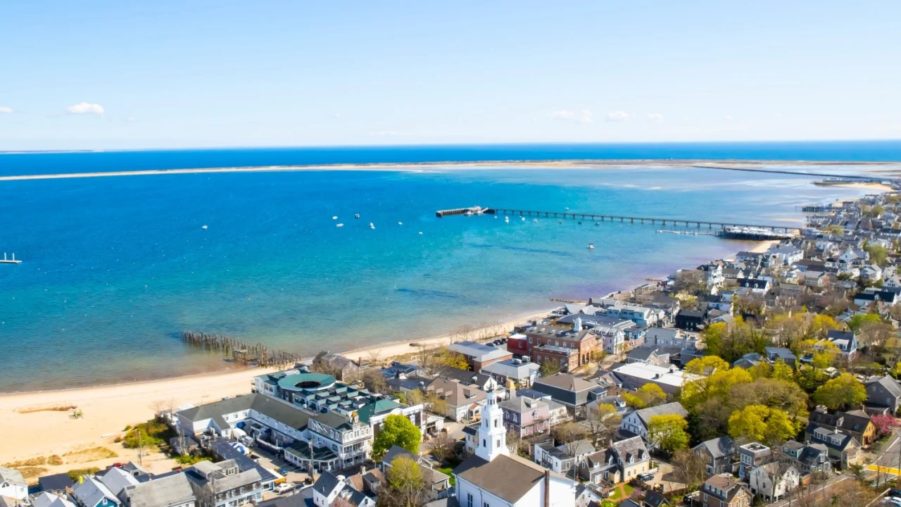 Provincetown, Massachusetts, United States - May 3th, 2023 : View of the harbour located next to the buildings of Provincetown. There is a blue sky. A sandy beach is located along the shore.