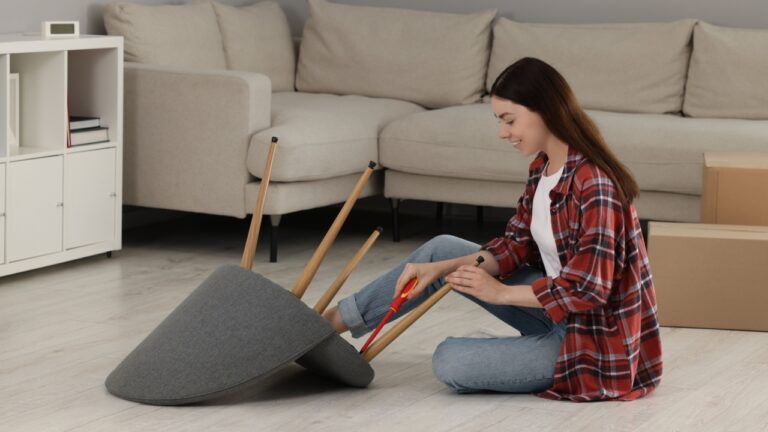 Young woman with screwdriver assembling armchair on floor at home