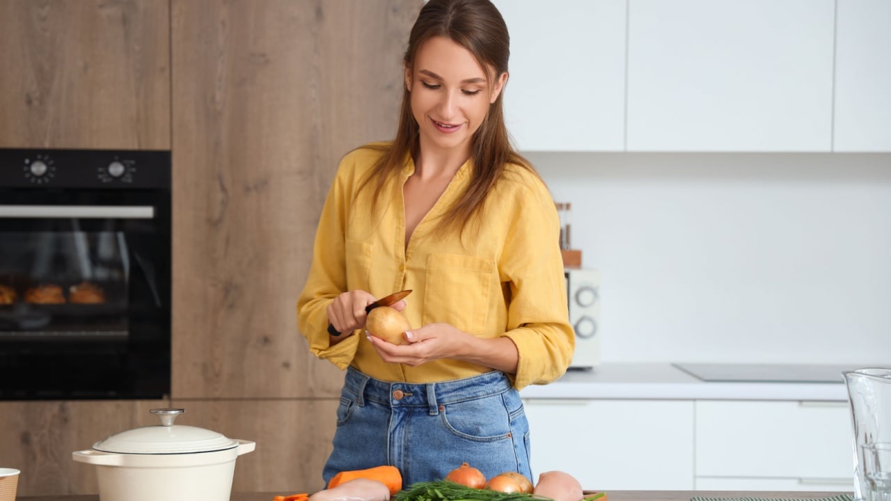 Young woman peeling potato for chicken soup in kitchen