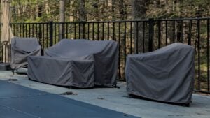 outdoor furniture covered for the season (end of year, winter) along with pool with cover (safety) chairs, sofa, couch, swimming pool, patio, back yard, stone, granite, protetive rain cover, sheath