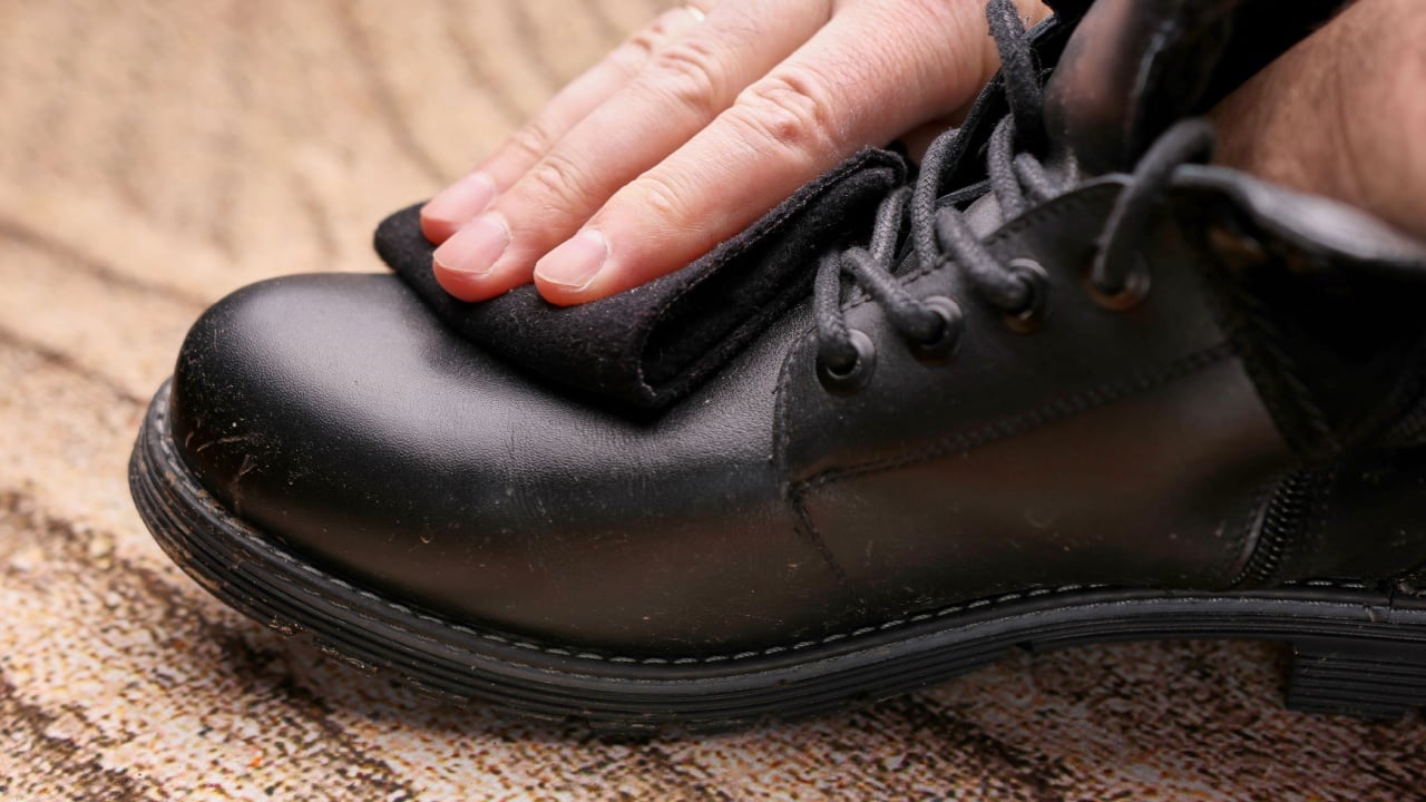 Black leather boots are cleaned of dirt with a woolen cloth. The concept of shoe care.