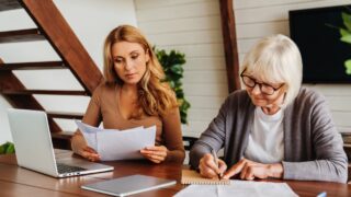Senior woman with help of her daughter making bills at home, paying loan, debt, filling in medical insurance, mortgage documents, health insurance