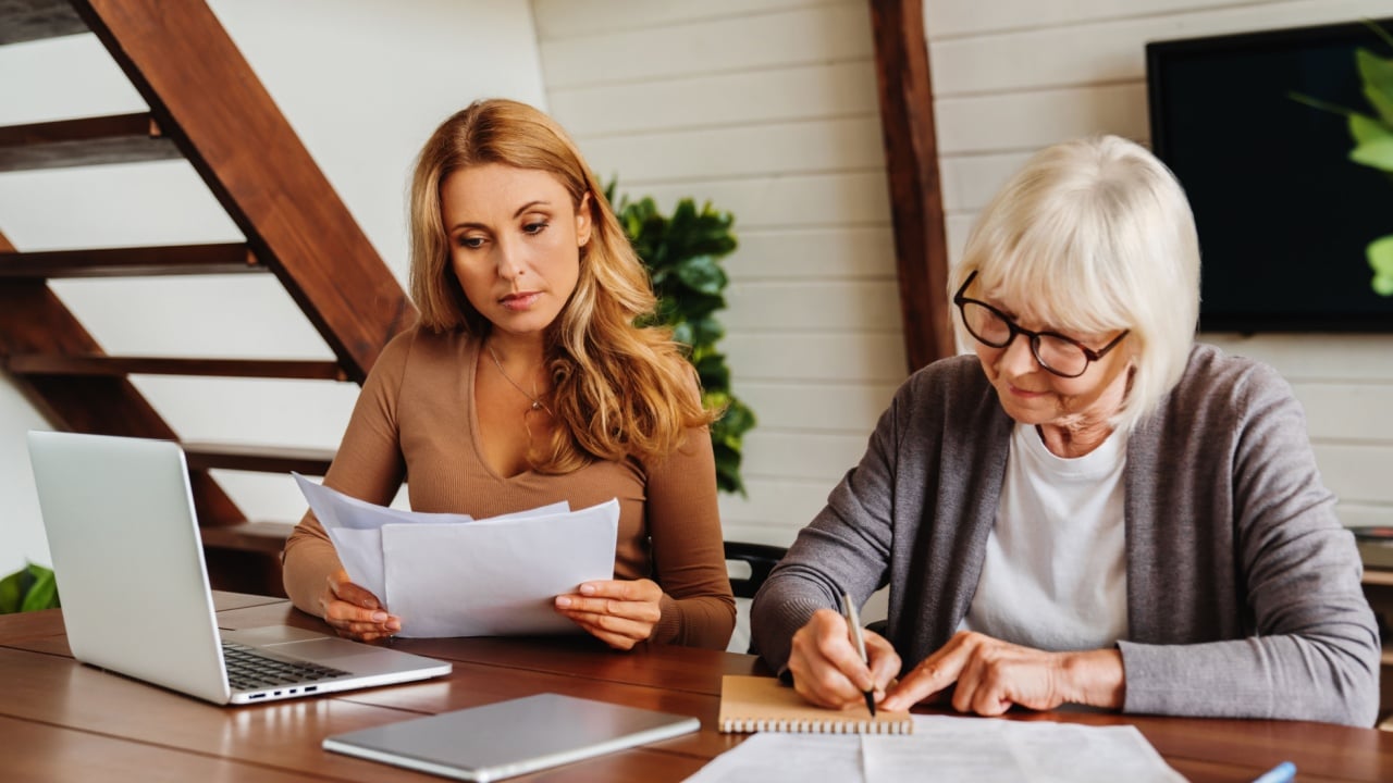 Senior woman with help of her daughter making bills at home, paying loan, debt, filling in medical insurance, mortgage documents, health insurance