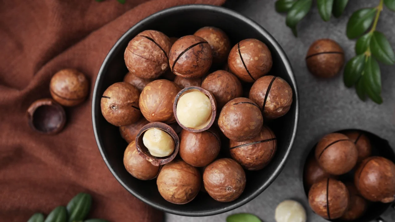 Tasty Macadamia nuts and green twigs on brown table, flat lay