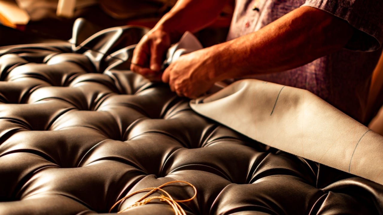 Hands of an upholsterer working on the upholstery of a tufted headboard