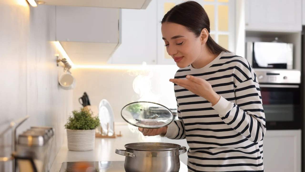 Beautiful woman smelling aromatic soup in kitchen