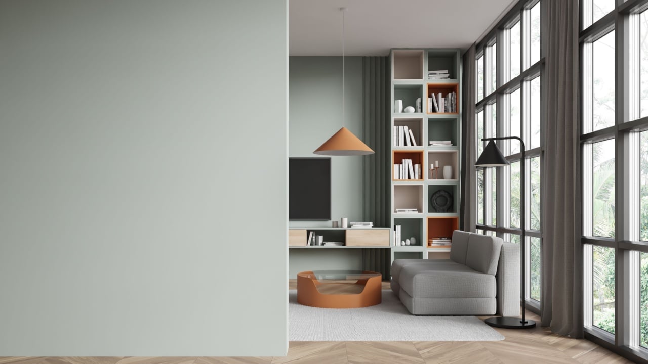 Interior of modern living room with green walls, wooden floor, comfortable gray sofa standing near wall mounted TV set and bookcase near panoramic window. Copy space wall on the left.