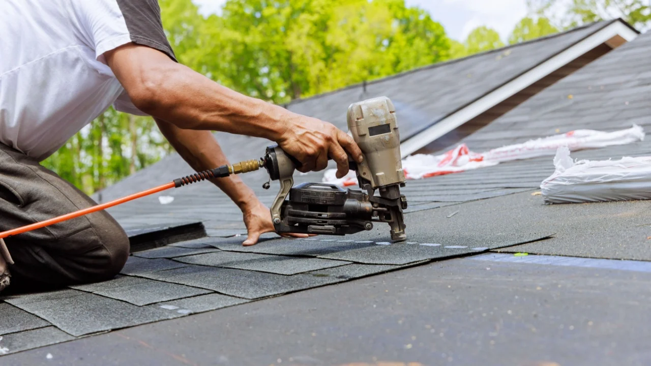 In addition to using an air pneumatic nail gun, roofer installs new asphalt bitumen shingles