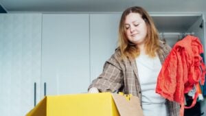 Woman selecting clothes from her wardrobe for recycling, donating to a Charity shop. Decluttering, Sorting clothes, Cleaning Up. Reuse, second hand concept. Conscious consumer, sustainable lifestyle.