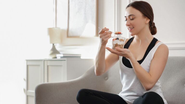 Woman eating tasty granola with fresh berries and yogurt on sofa at home