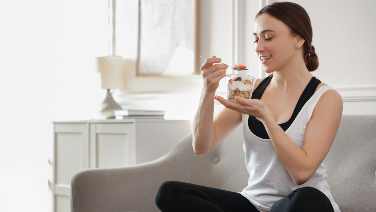 Woman eating tasty granola with fresh berries and yogurt on sofa at home