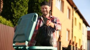 Man throwing trash bag full of garbage into bin outdoors.