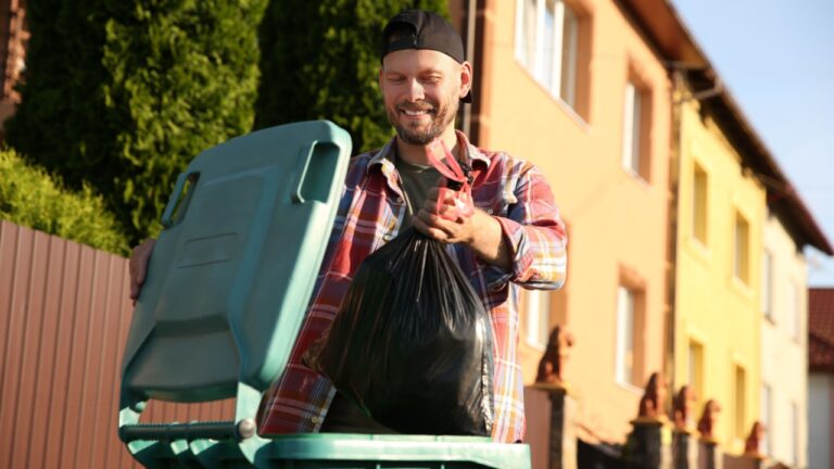Man throwing trash bag full of garbage into bin outdoors.