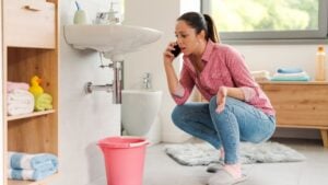 Woman calling a professional plumber at home using her smartphone, her bathroom sink is leaking