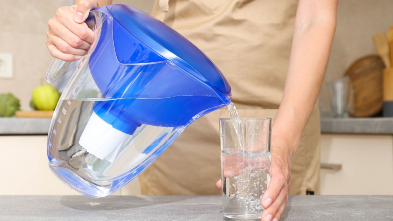 A water filter stands in the kitchen with a glass of water