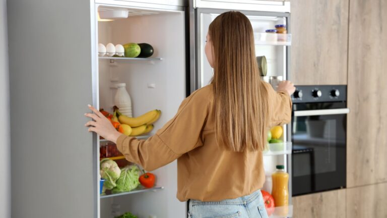 Young woman near open fridge in kitchen.