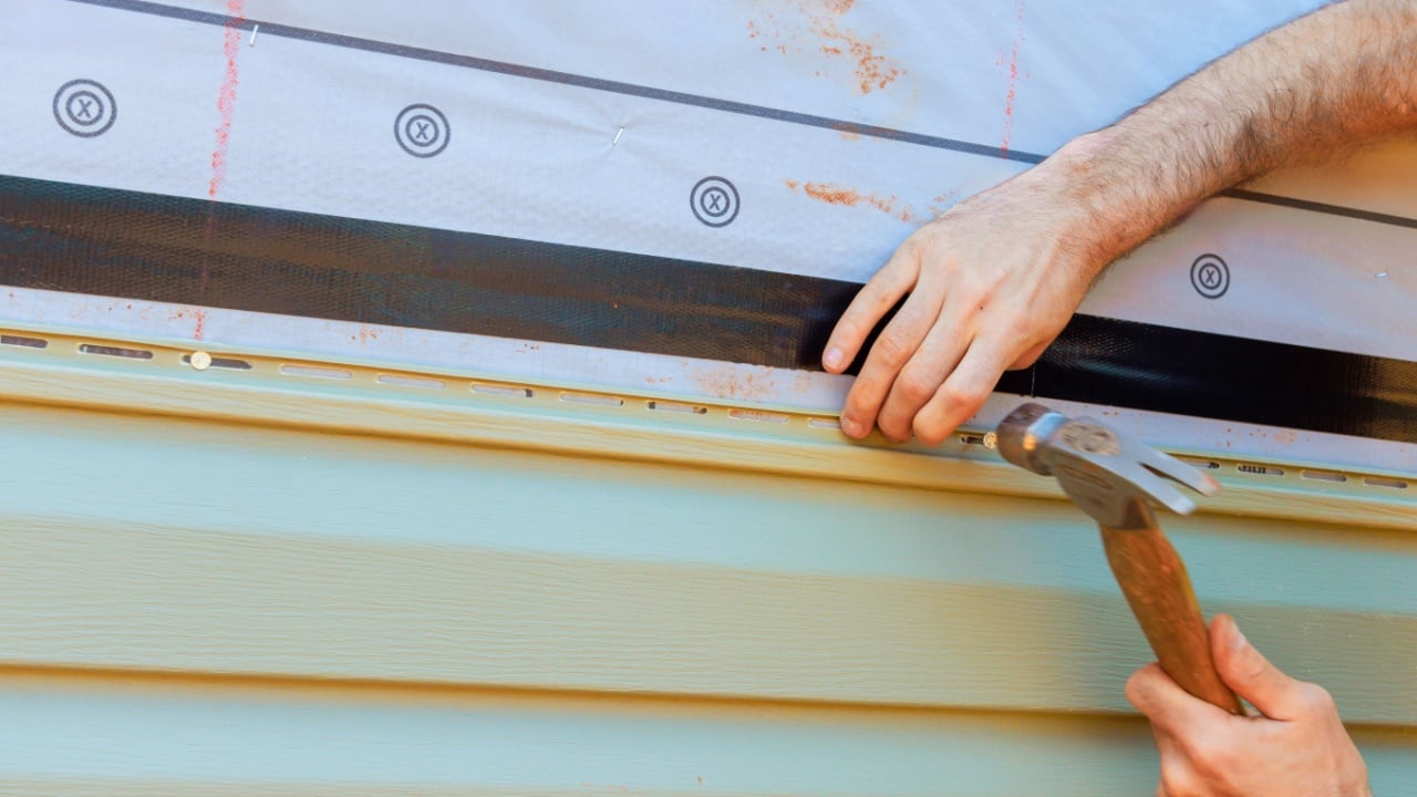 Craftsperson installing siding using hammer careful techniques on residential building in vinyl siding broad