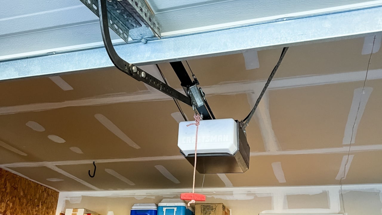 Broomfield, Colorado, USA-September 15, 2023-A garage door opener installed on the ceiling with a red emergency release cord hanging below An LED light fixture is mounted nearby providing bright