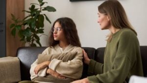 Portrait of troubled teenage girl looking away from parent while sitting on couch during family therapy session