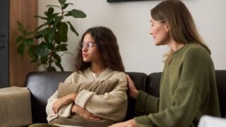 Portrait of troubled teenage girl looking away from parent while sitting on couch during family therapy session