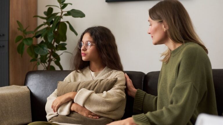 Portrait of troubled teenage girl looking away from parent while sitting on couch during family therapy session
