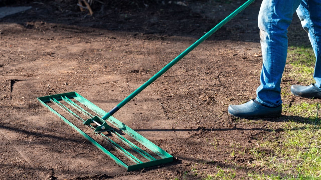 Man uses a lawn rake to level the ground in the garden to even out any unevenness and prepare the ground for a perfect lawn.