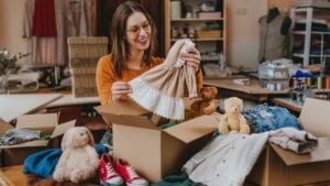 Woman sorting an old out-of-use kid clothes and shoes in box for charity or converting discarded materials. Upcycling concept.