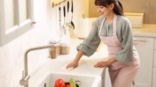 Smiling woman cleaning countertop with paper towel in kitchen