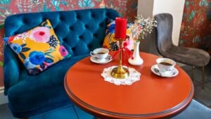 Vibrant Cafe Corner with Blue Velvet Sofa and Orange Table.Cozy Coffee Setting with Floral Wallpaper and Navy Tufted Loveseat.