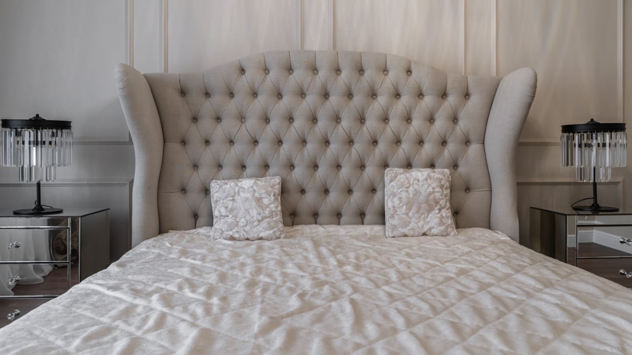 bedroom design with a double bed, large upholstered headboard. the lamp on the bedside table. a lamp with crystals. elegant interior. a photo of a bedroom in beige shades.
